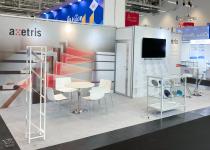 Stand for Axetris, single back wall with integrated store room, tables & chairs, and display counter